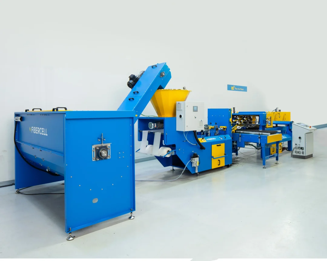 A blue industrial machine labeled "FIBERCELL" processes materials in a spacious, clean factory setting. It features conveyors and control panels, adjacent to a sign reading "Blue Rock Plant".