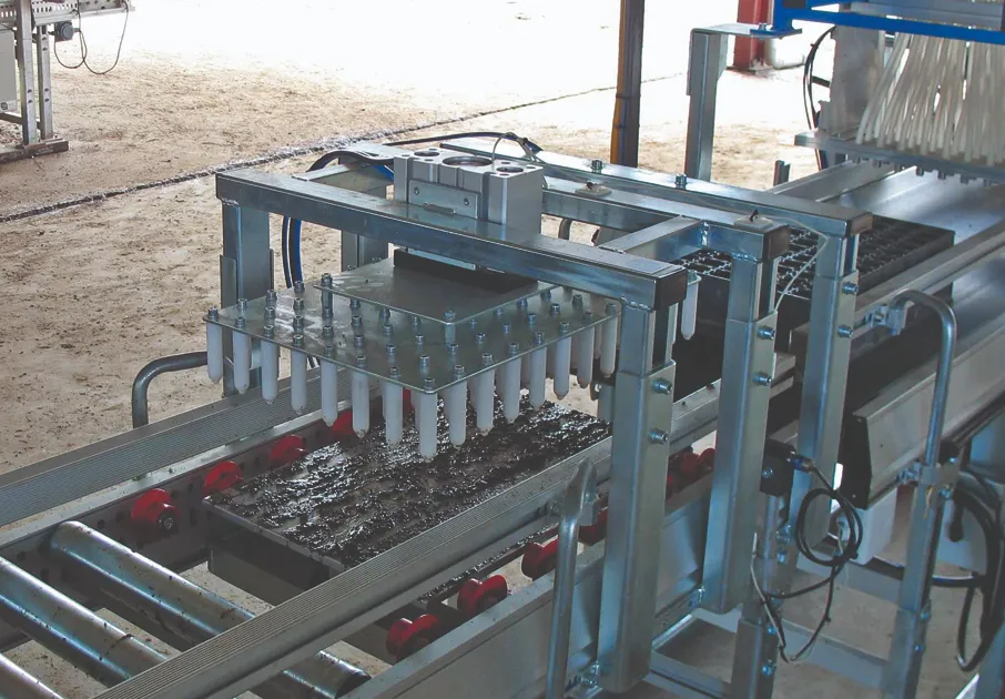 A seeding machine is inserting soil plugs into trays using multiple nozzles, operating on a conveyor in an industrial setting.